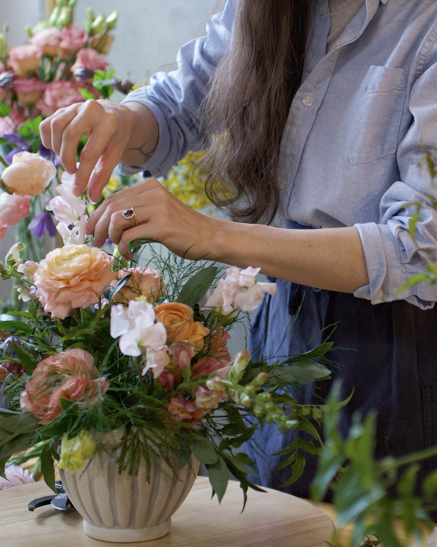 Adore Flowers designer arranging a custom florist's choice arrangement of peach ranunculus, garden roses and sweet peas in a ceramic vase, Los Angeles studio