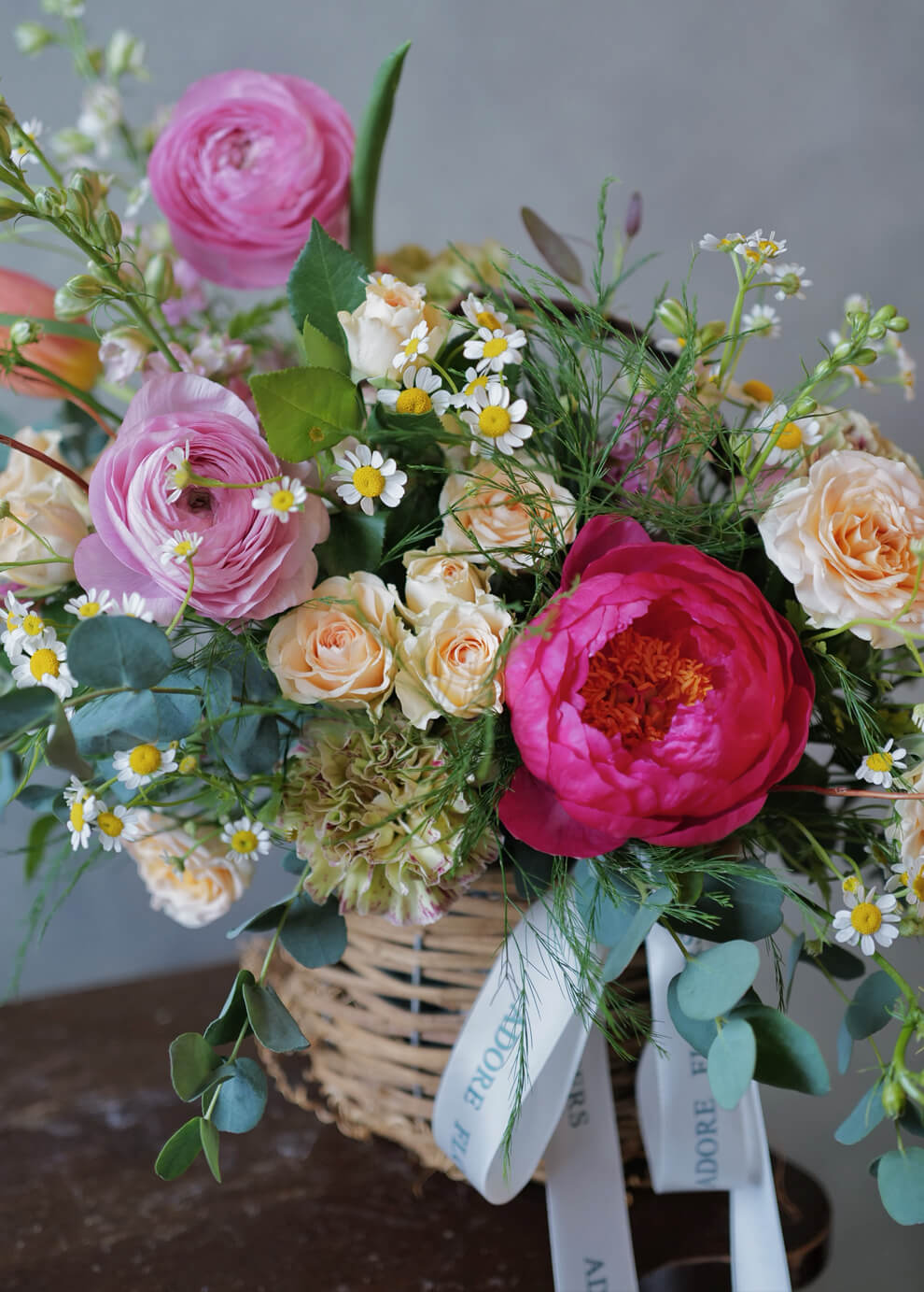 Close-up of vibrant pink peony bloom with yellow chamomile and delicate greenery in spring basket—flower delivery Philadelphia