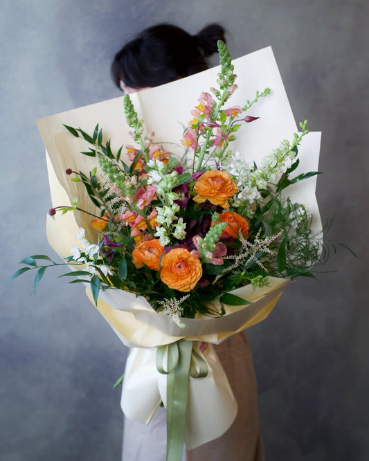 Wildflower bouquet hand-tied in wrap, orange ranunculus and snapdragon with wild greenery, The Wild Bunch by Adore Flowers Los Angeles
