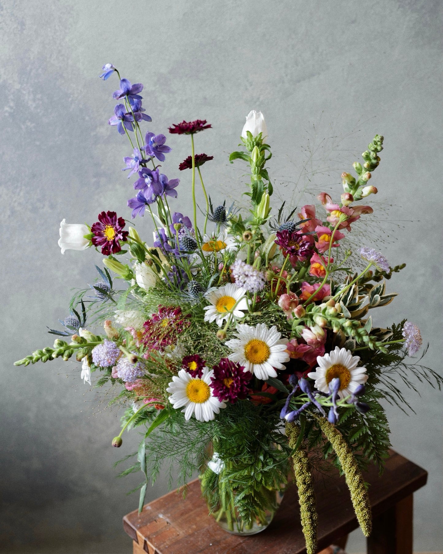 Wildflower vase arrangement variation with daisies, blue delphinium, scabiosa and snapdragons in a glass vase, The Wild Bunch by Adore Flowers Los Angeles