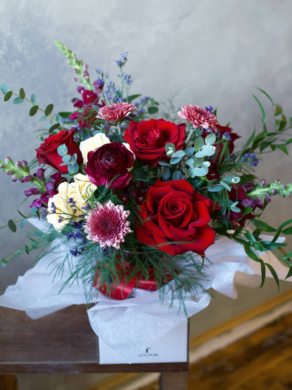 Bouquet of red and white flowers in a clear vase on a wooden table.
