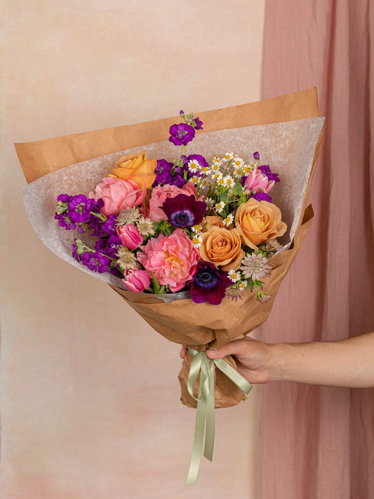 A bright birthday arrangement of pink and purple peonies, tulips, roses, and anemones
