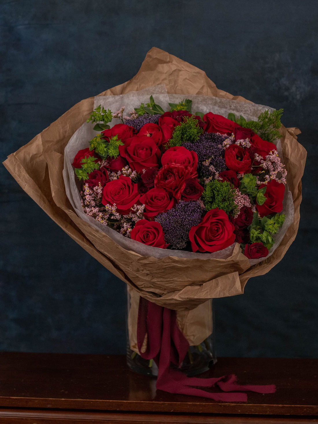 A hand-tied Adore Flowers bouquet of red roses, mini roses, and ranunculus wrapped for delivery