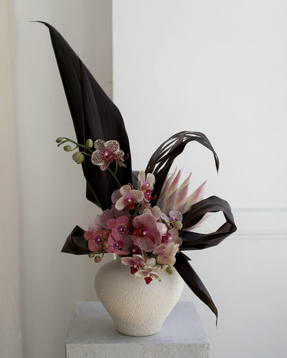 Custom designer arrangement, florist's choice with spotted phalaenopsis orchids, king protea and dark cordyline leaves in a textured white vase, Adore Flowers Los Angeles