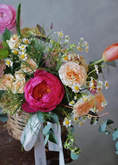 Mid-range shot showing pink ranunculus, pastel spray roses, chamomile & eucalyptus in a woven basket—Adore Flowers Philadelphia